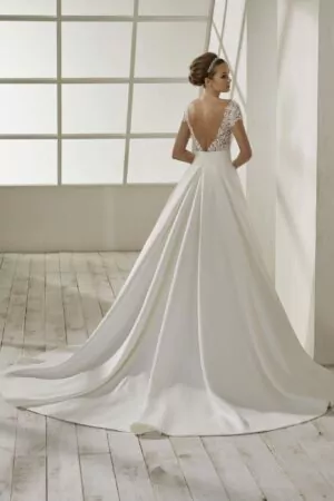 Robe de mariée en crêpe blanche avec corsage en dentelle, manches courtes, dos plongeant et jupe fluide avec traîne légère.