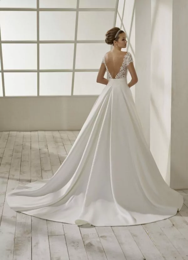 Robe de mariée en crêpe blanche avec corsage en dentelle, manches courtes, dos plongeant et jupe fluide avec traîne légère.