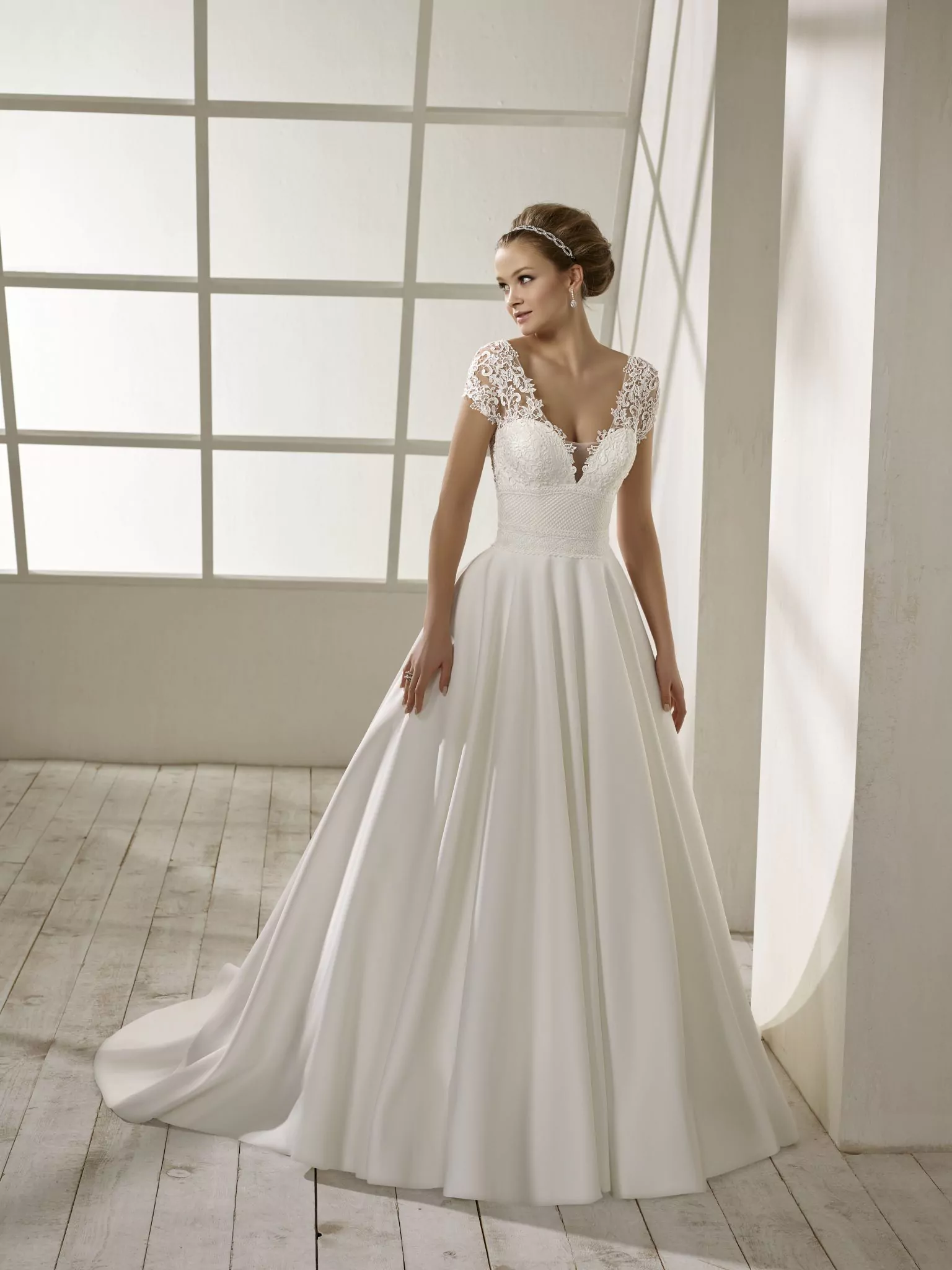 Robe de mariée en crêpe blanche avec corsage en dentelle, manches courtes, dos plongeant et jupe fluide avec traîne légère.