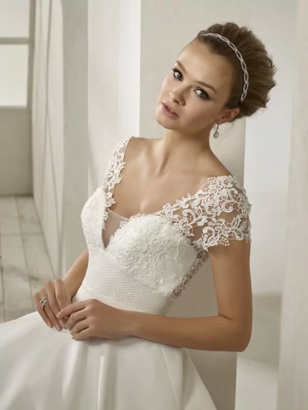 Robe de mariée en crêpe blanche avec corsage en dentelle, manches courtes, dos plongeant et jupe fluide avec traîne légère.