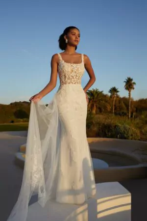 Robe de mariée en dentelle avec dos plongeant et surjupe transparente brodée, photographiée dans un jardin au coucher du soleil.