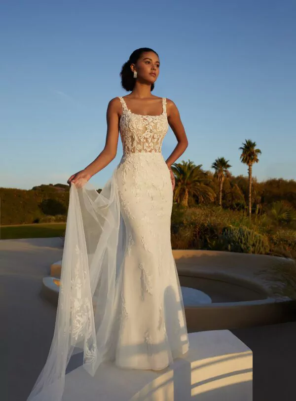 Robe de mariée en dentelle avec dos plongeant et surjupe transparente brodée, photographiée dans un jardin au coucher du soleil.