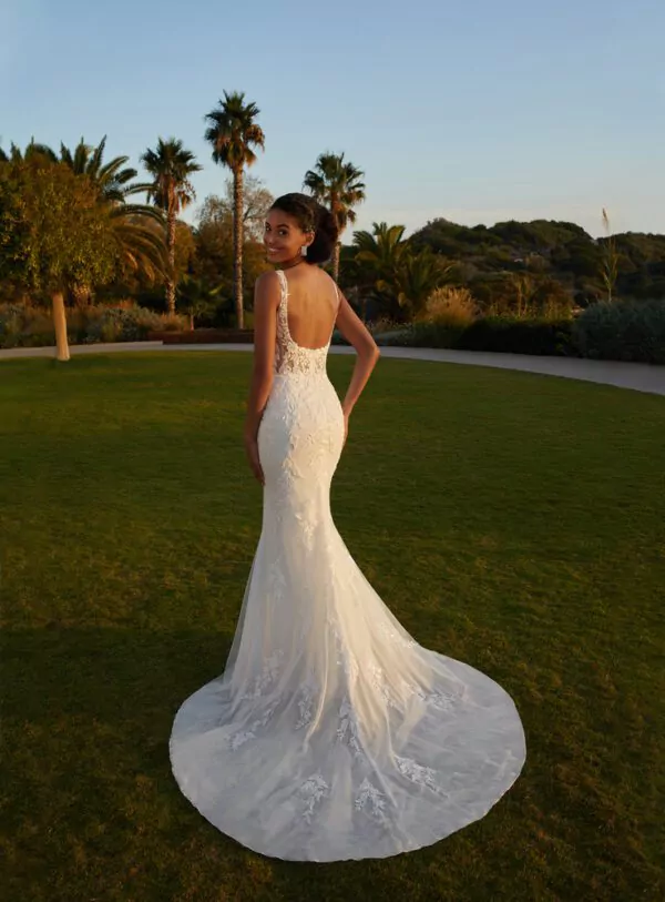 Robe de mariée en dentelle avec dos plongeant et surjupe transparente brodée, photographiée dans un jardin au coucher du soleil.