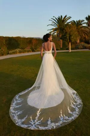 Robe de mariée en dentelle avec dos plongeant et surjupe transparente brodée, photographiée dans un jardin au coucher du soleil.