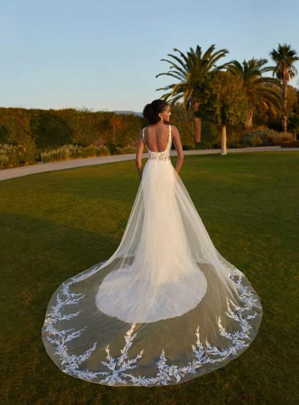 Robe de mariée en dentelle avec dos plongeant et surjupe transparente brodée, photographiée dans un jardin au coucher du soleil.