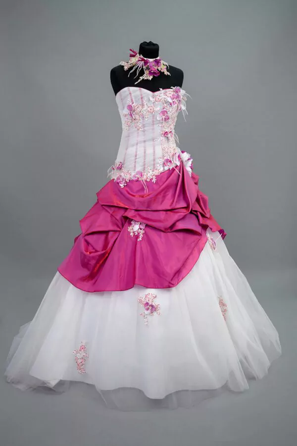 Robe de mariée Allure Annie Couture en blanc et fuchsia, avec un bustier drapé en tulle, des détails floraux et une jupe volumineuse, idéale pour un mariage audacieux et mémorable.