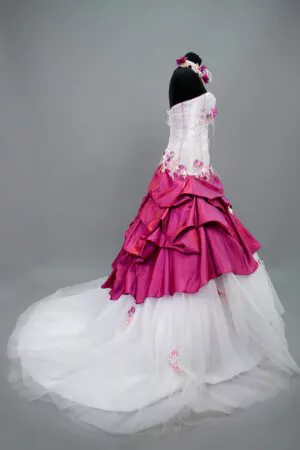 Robe de mariée Allure Annie Couture en blanc et fuchsia, avec un bustier drapé en tulle, des détails floraux et une jupe volumineuse, idéale pour un mariage audacieux et mémorable.