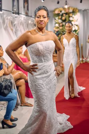 Robe de mariée bustier coupe sirène, ornée de sequins et perles, présentée sur un tapis rouge lors d’un défilé.