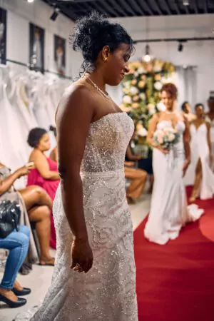 Robe de mariée bustier coupe sirène, ornée de sequins et perles, présentée sur un tapis rouge lors d’un défilé.