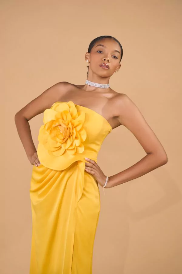 Robe jaune bustier ornée d'une grande fleur sculpturale et d'une fente élégante, idéale pour les événements prestigieux.