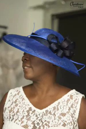 Femme portant un large bibi en sisal bleu royal avec un nœud noir, idéal pour les mariages et les événements formels.