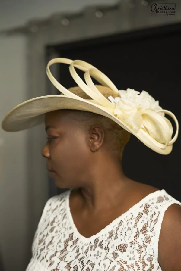 Chapeau en paille ivoire avec boucles et fleurs, conçu artisanalement par Christiane Boutique. Pièce unique pour une élégance intemporelle.